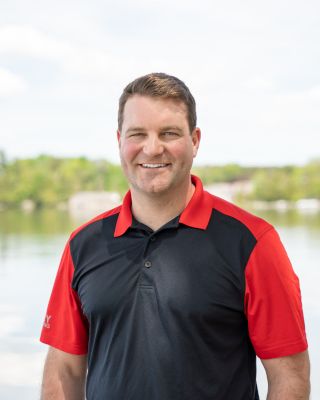 A man standing in front of water wearing a red and black shirt.